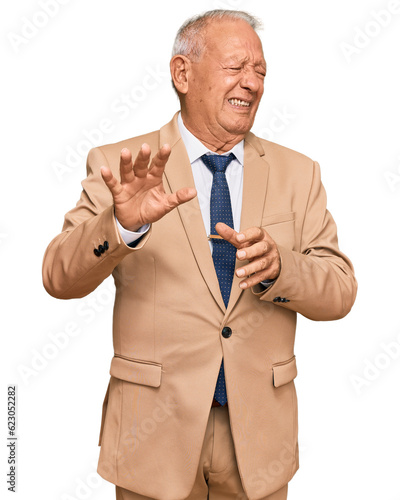 Senior caucasian man wearing business suit and tie disgusted expression, displeased and fearful doing disgust face because aversion reaction. with hands raised