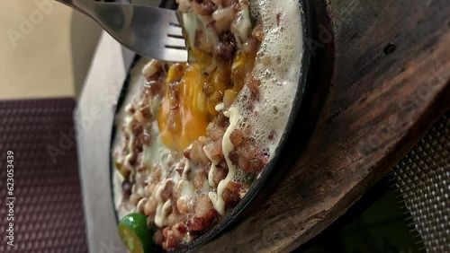 Mixing raw egg with pork sisig in a sizzling plate, authentic traditional Filipino dish