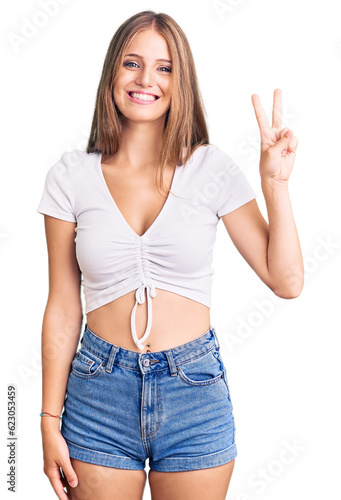Young beautiful blonde woman wearing casual white tshirt showing and pointing up with fingers number two while smiling confident and happy.