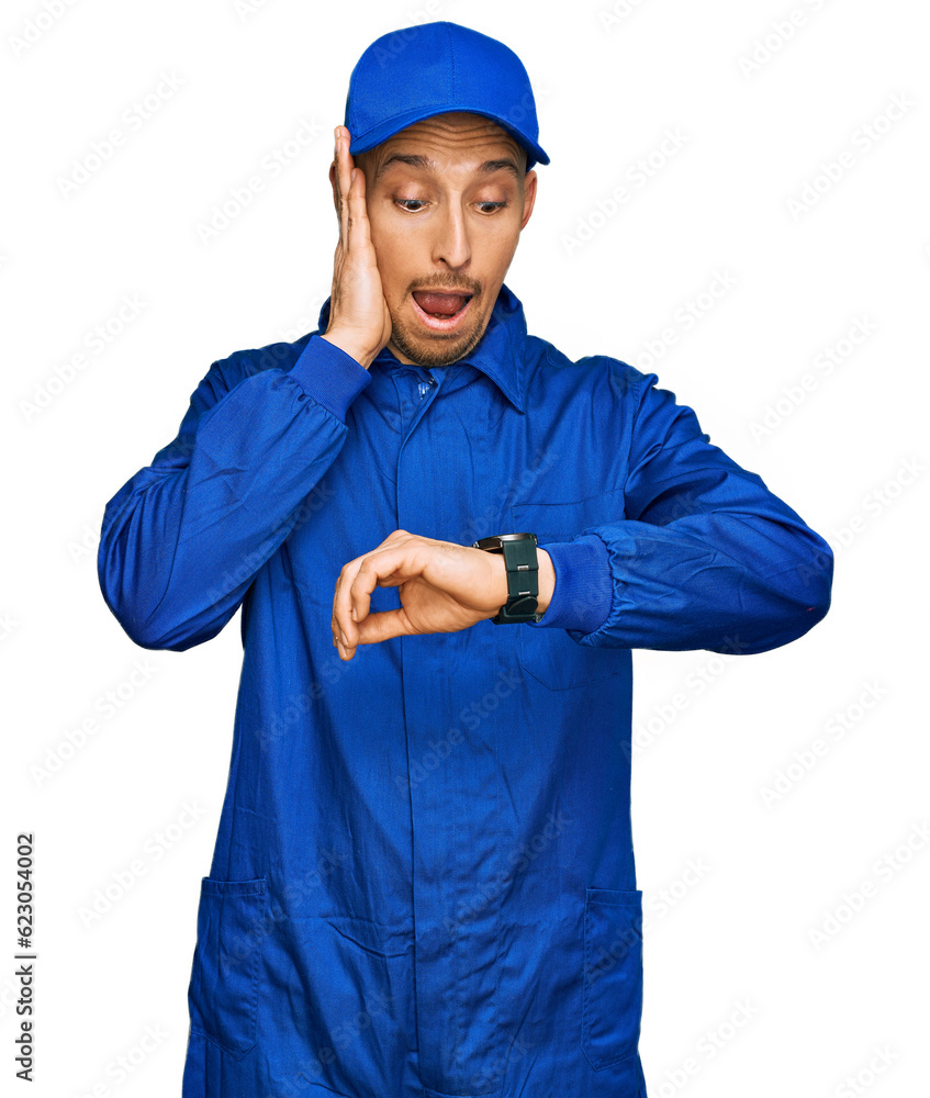 Bald man with beard wearing builder jumpsuit uniform looking at the watch time worried, afraid of getting late Bald man with beard wearing builder jumpsuit uniform looking at the watch time worried, afraid of getting late