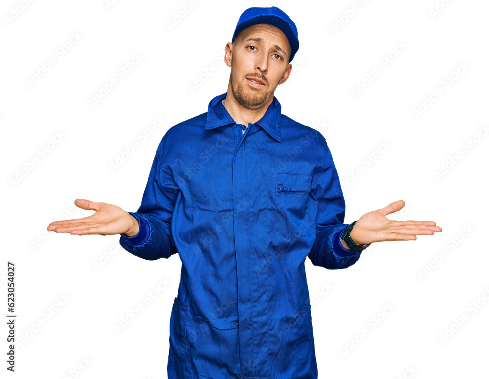 Bald man with beard wearing builder jumpsuit uniform clueless and confused with open arms, no idea concept. Bald man with beard wearing builder jumpsuit uniform clueless and confused with open arms, no idea concept.