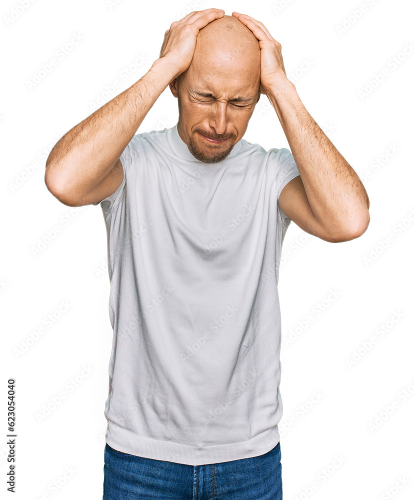 Bald man with beard wearing casual white t shirt suffering from headache desperate and stressed because pain and migraine. hands on head. Bald man with beard wearing casual white t shirt suffering from headache desperate and stressed because pain and migraine. hands on head.