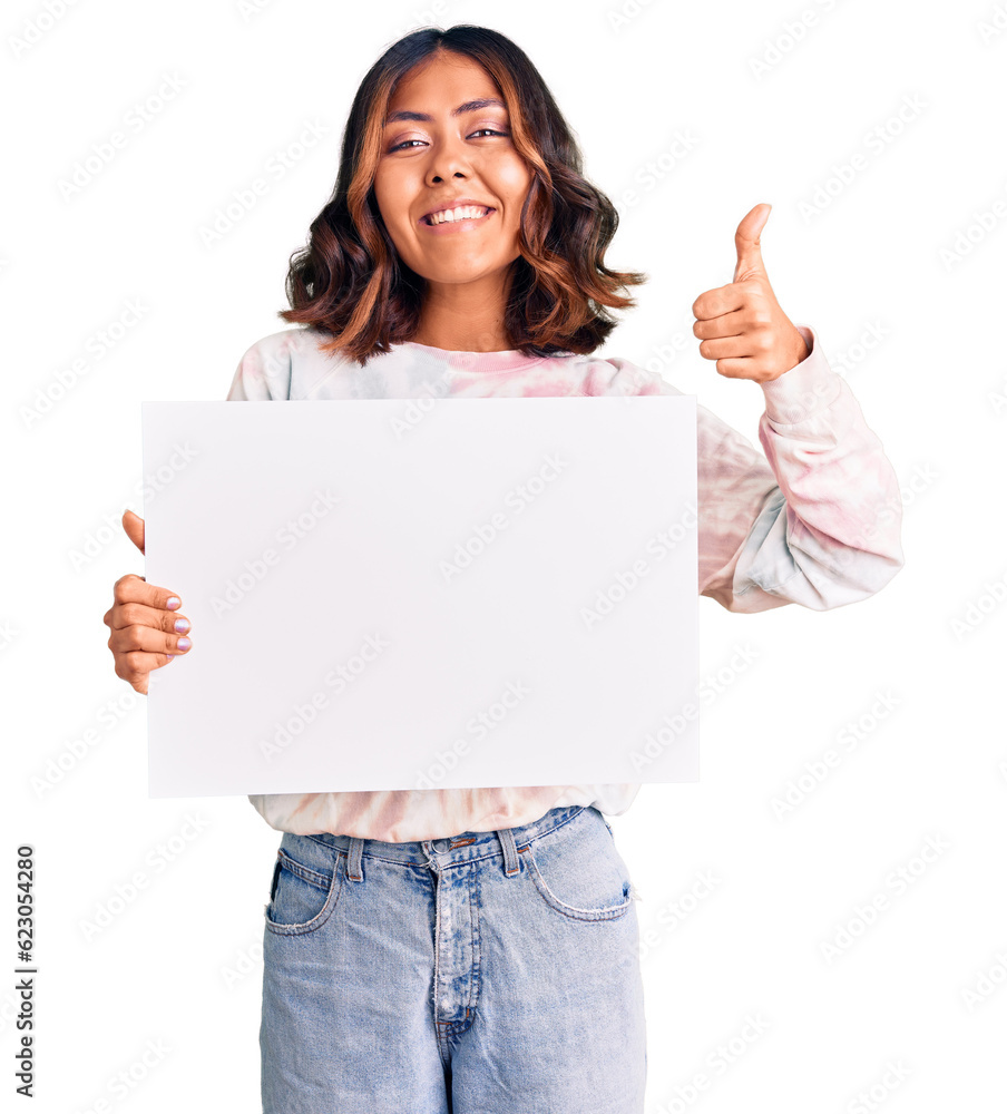 Young beautiful mixed race woman holding cardboard banner with blank space smiling happy and positive, thumb up doing excellent and approval sign Young beautiful mixed race woman holding cardboard banner with blank space smiling happy and positive, thumb up doing excellent and approval sign