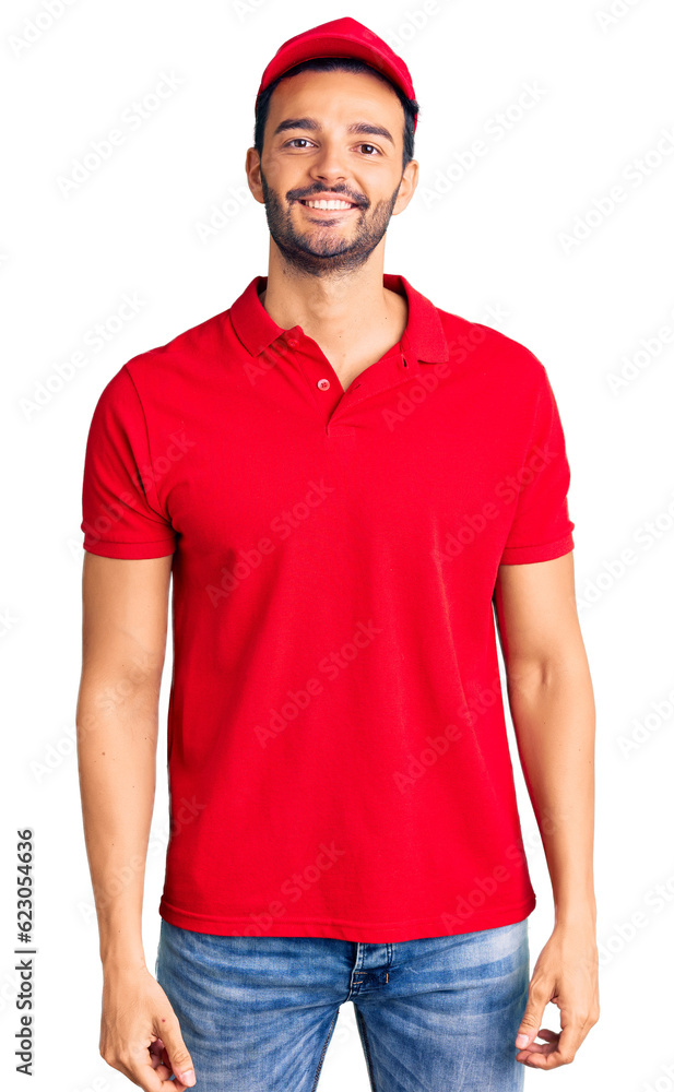 Young handsome hispanic man wearing delivery courier uniform looking positive and happy standing and smiling with a confident smile showing teeth Young handsome hispanic man wearing delivery courier uniform looking positive and happy standing and smiling with a confident smile showing teeth