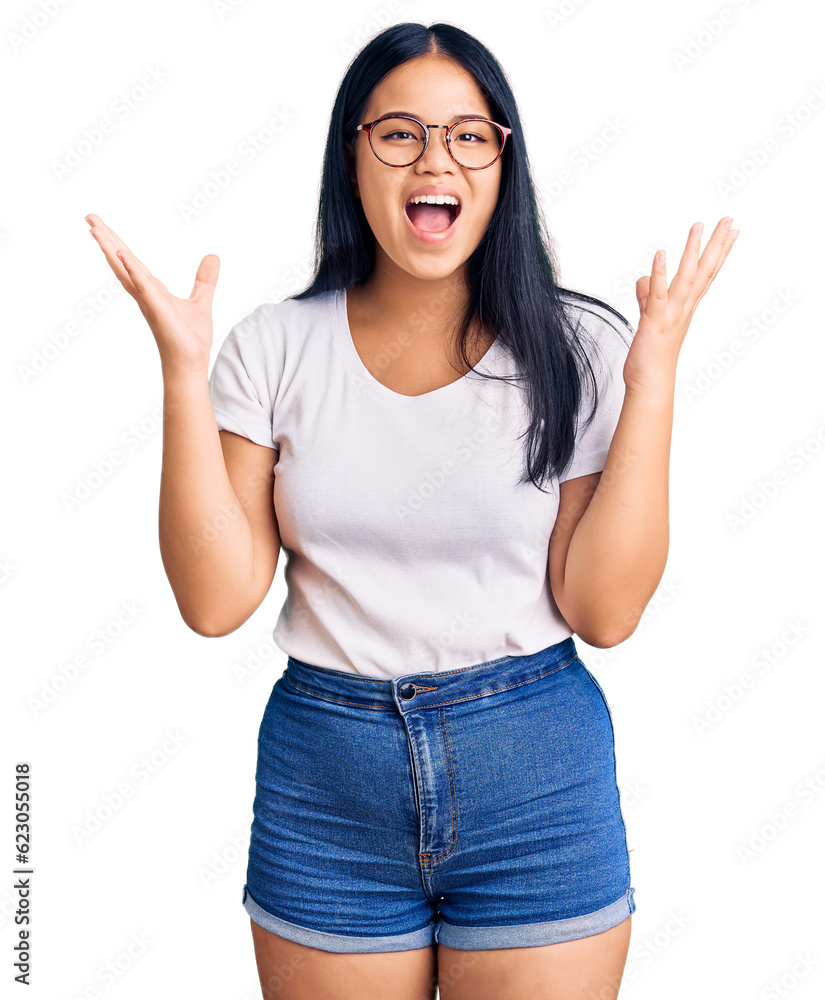 Young beautiful asian girl wearing casual clothes and glasses celebrating crazy and amazed for success with arms raised and open eyes screaming excited. winner concept Young beautiful asian girl wearing casual clothes and glasses celebrating crazy and amazed for success with arms raised and open eyes screaming excited. winner concept