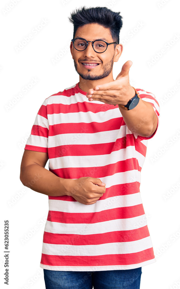 Handsome latin american young man wearing casual clothes and glasses smiling friendly offering handshake as greeting and welcoming. successful business. Handsome latin american young man wearing casual clothes and glasses smiling friendly offering handshake as greeting and welcoming. successful business.