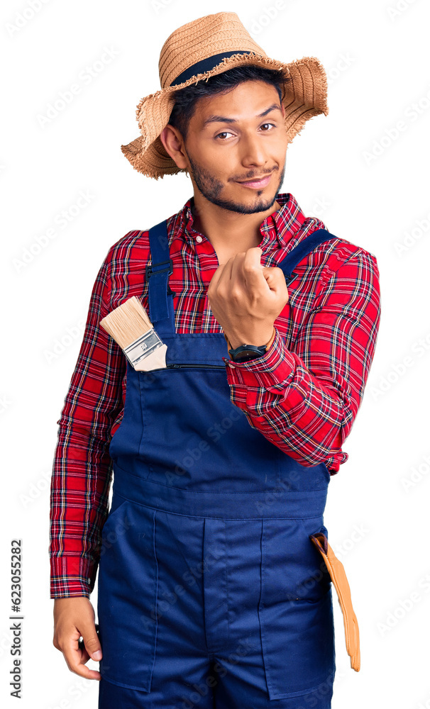 Handsome latin american young man weaing handyman uniform beckoning come here gesture with hand inviting welcoming happy and smiling Handsome latin american young man weaing handyman uniform beckoning come here gesture with hand inviting welcoming happy and smiling