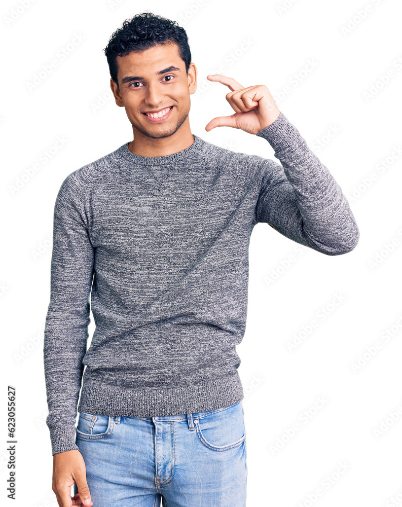 Hispanic handsome young man wearing casual sweater smiling and confident gesturing with hand doing small size sign with fingers looking and the camera. measure concept. Hispanic handsome young man wearing casual sweater smiling and confident gesturing with hand doing small size sign with fingers looking and the camera. measure concept.