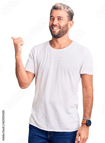 Young handsome blond man wearing casual t-shirt amazed and surprised looking up and pointing with fingers and raised arms.