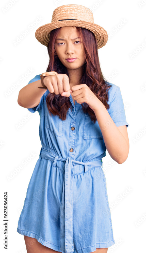 Young beautiful chinese girl wearing summer hat punching fist to fight, aggressive and angry attack, threat and violence Young beautiful chinese girl wearing summer hat punching fist to fight, aggressive and angry attack, threat and violence