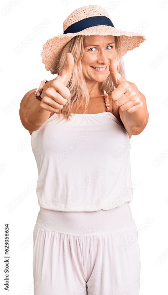 Middle age fit blonde woman wearing summer hat approving doing positive gesture with hand, thumbs up smiling and happy for success. winner gesture. Middle age fit blonde woman wearing summer hat approving doing positive gesture with hand, thumbs up smiling and happy for success. winner gesture.