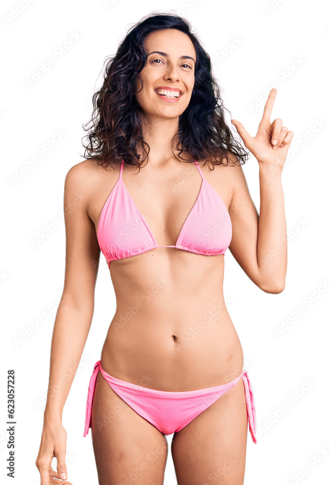Young beautiful hispanic woman wearing bikini with a big smile on face, pointing with hand finger to the side looking at the camera. - obrazy, fototapety, plakaty 