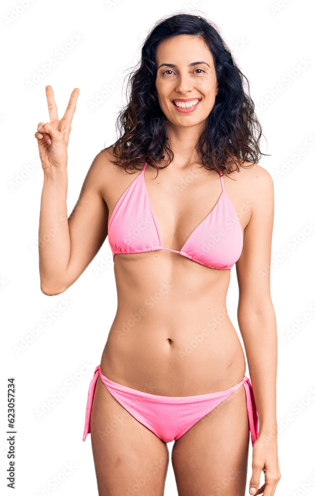 Young beautiful hispanic woman wearing bikini smiling looking to the camera showing fingers doing victory sign. number two. Young beautiful hispanic woman wearing bikini smiling looking to the camera showing fingers doing victory sign. number two.
