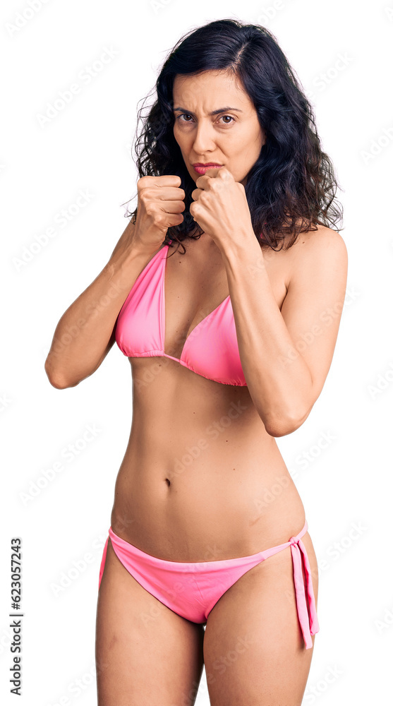 Naklejka premium Young beautiful hispanic woman wearing bikini ready to fight with fist defense gesture, angry and upset face, afraid of problem