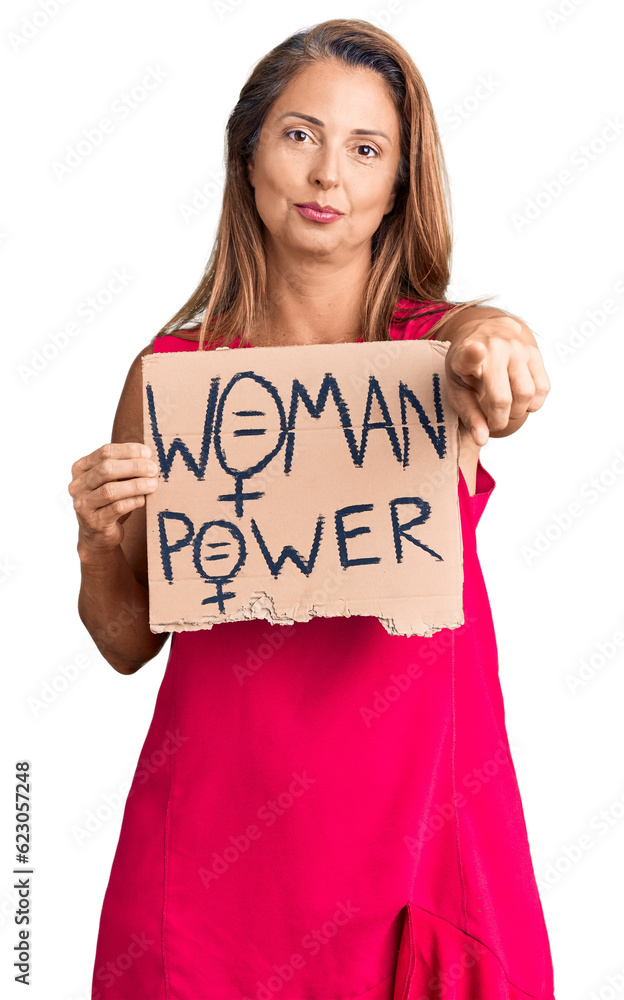 Middle age hispanic woman holding woman power banner pointing with finger to the camera and to you, confident gesture looking serious Middle age hispanic woman holding woman power banner pointing with finger to the camera and to you, confident gesture looking serious