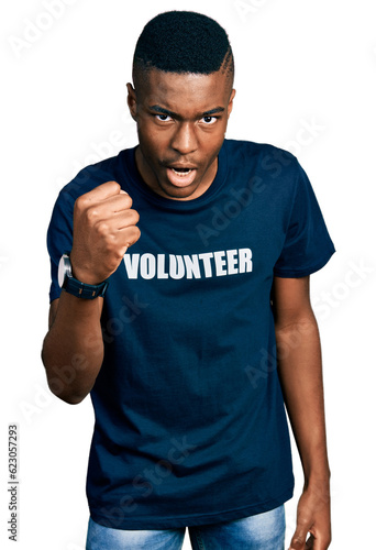 Young african american man wearing volunteer t shirt angry and mad raising fist frustrated and furious while shouting with anger. rage and aggressive concept.