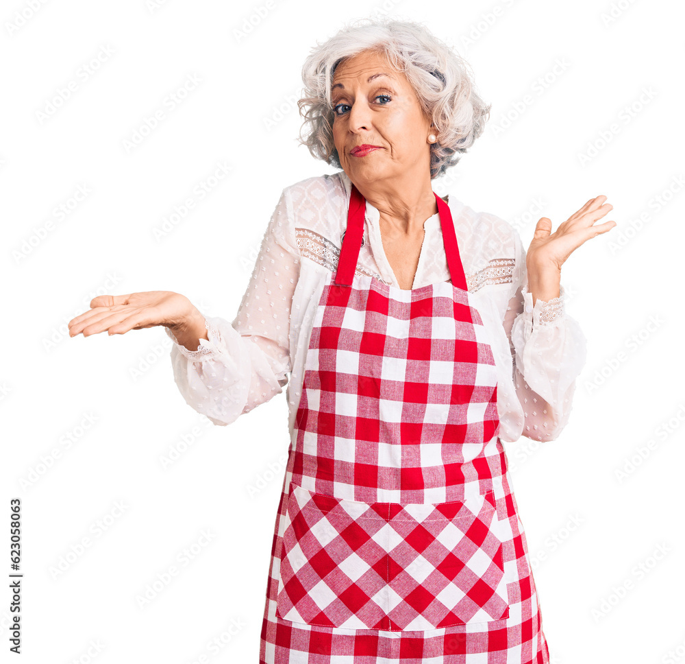 Senior grey-haired woman wearing apron clueless and confused expression with arms and hands raised. doubt concept. Senior grey-haired woman wearing apron clueless and confused expression with arms and hands raised. doubt concept.