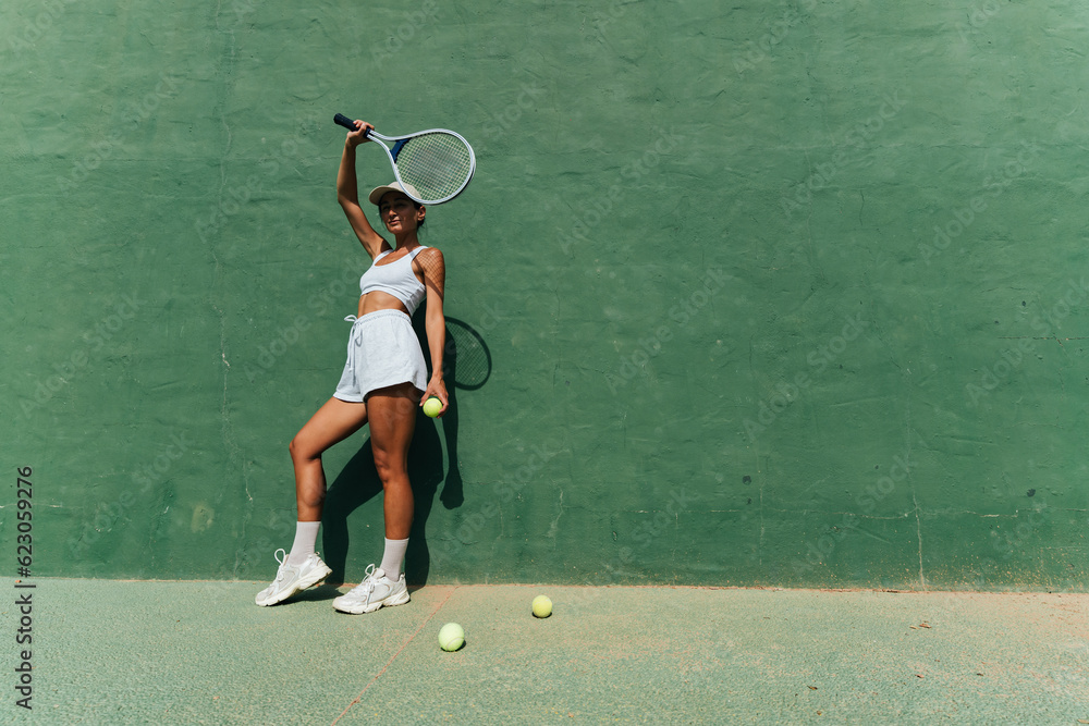 beautiful girl in a cap plays tennis on the tennis court against the background of a green wall