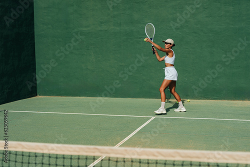 beautiful girl in a cap plays tennis on the tennis court against the background of a green wall © sutulastock