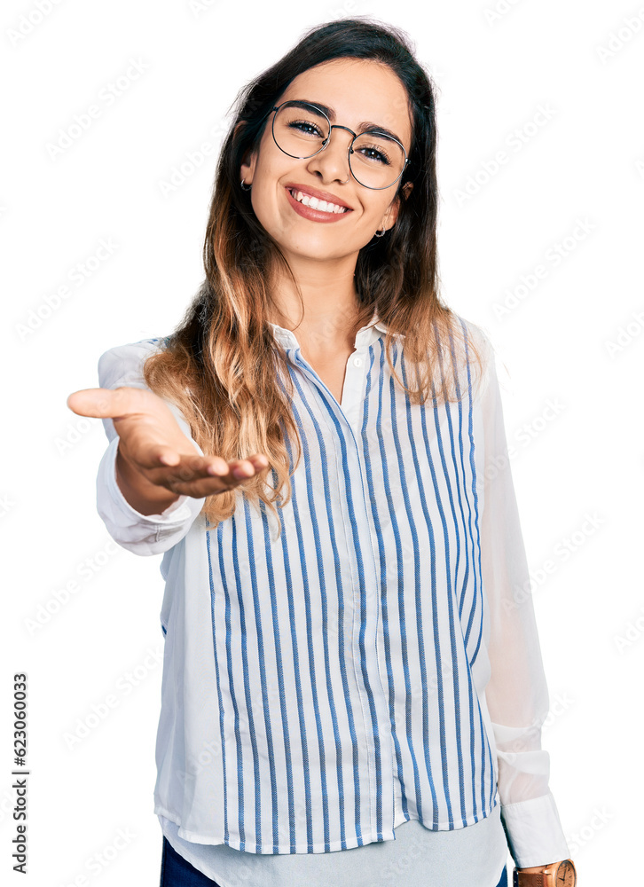 Beautiful hispanic woman wearing casual striped shirt smiling friendly offering handshake as greeting and welcoming. successful business. Beautiful hispanic woman wearing casual striped shirt smiling friendly offering handshake as greeting and welcoming. successful business.