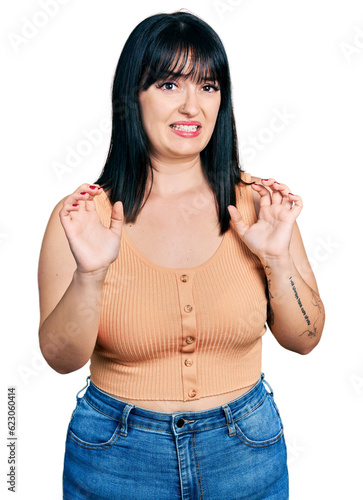 Young hispanic plus size woman wearing casual clothes afraid and terrified with fear expression stop gesture with hands, shouting in shock. panic concept.