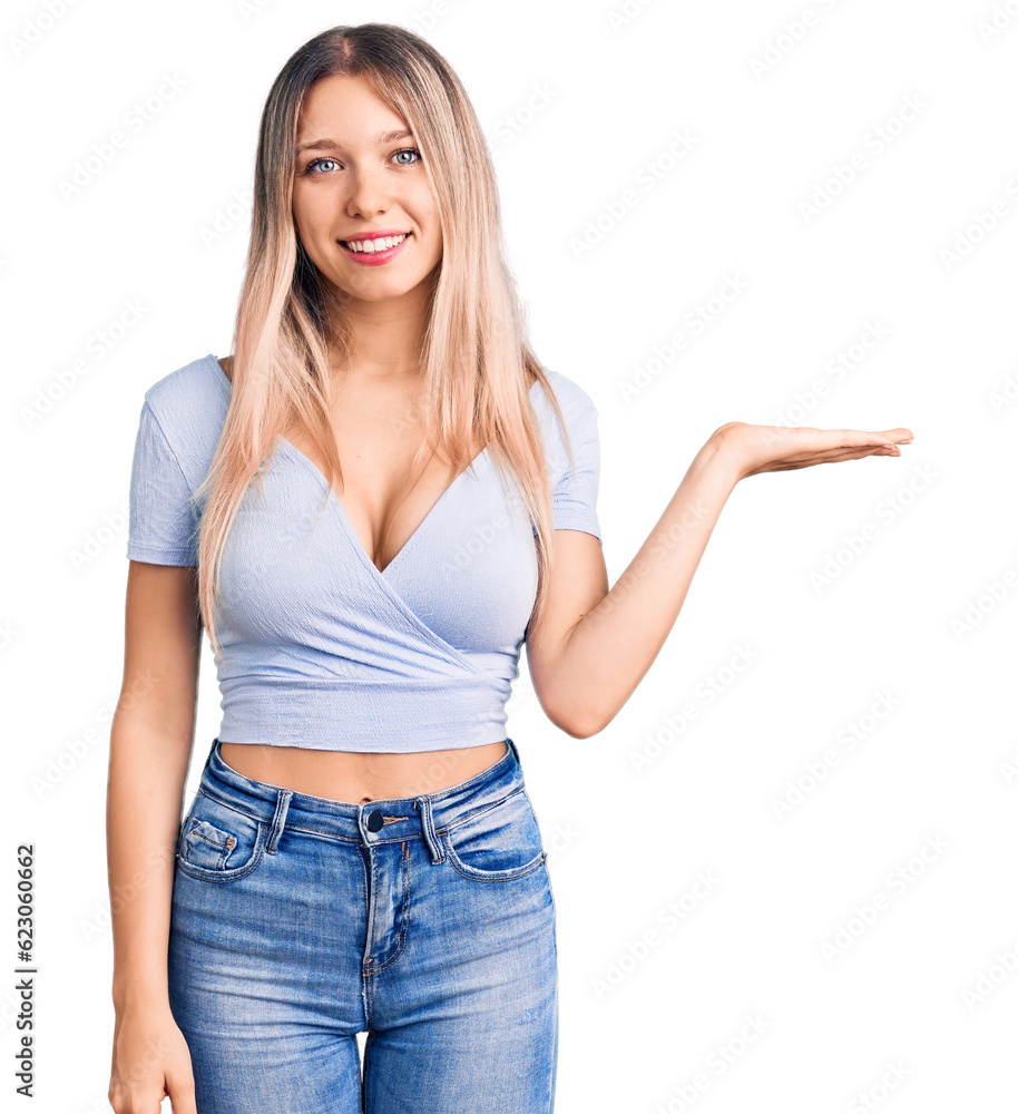 Young beautiful blonde woman wearing casual clothes smiling cheerful presenting and pointing with palm of hand looking at the camera. Young beautiful blonde woman wearing casual clothes smiling cheerful presenting and pointing with palm of hand looking at the camera.