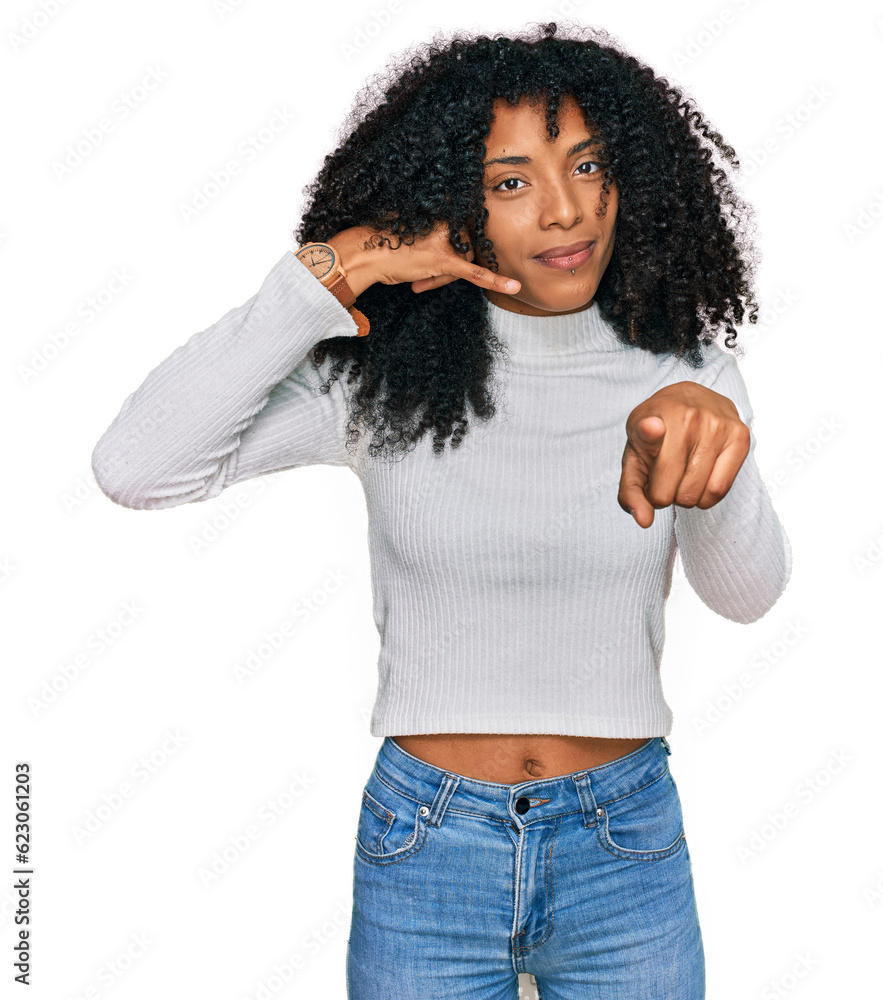 Young african american girl wearing casual clothes smiling doing talking on the telephone gesture and pointing to you. call me. Young african american girl wearing casual clothes smiling doing talking on the telephone gesture and pointing to you. call me.