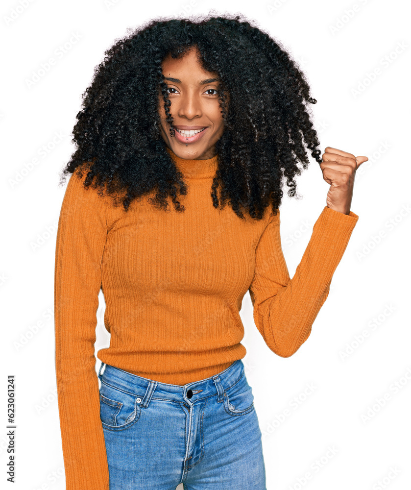 Young african american girl wearing casual clothes smiling with happy face looking and pointing to the side with thumb up. Young african american girl wearing casual clothes smiling with happy face looking and pointing to the side with thumb up.