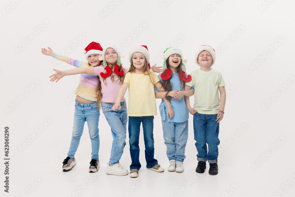 Merry Christmas and Happy New Year! A group of cheerful happy children in festive santa claus and elf hats on a white studio background. Children hug and have fun