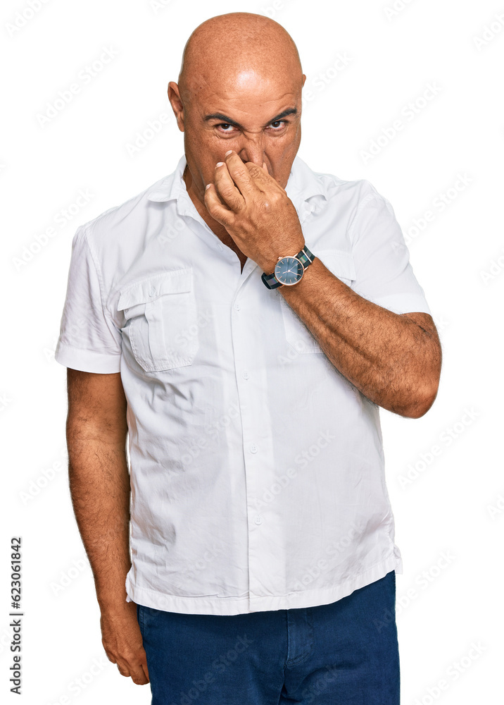 Mature middle east man with mustache wearing casual white shirt smelling something stinky and disgusting, intolerable smell, holding breath with fingers on nose. bad smell Mature middle east man with mustache wearing casual white shirt smelling something stinky and disgusting, intolerable smell, holding breath with fingers on nose. bad smell