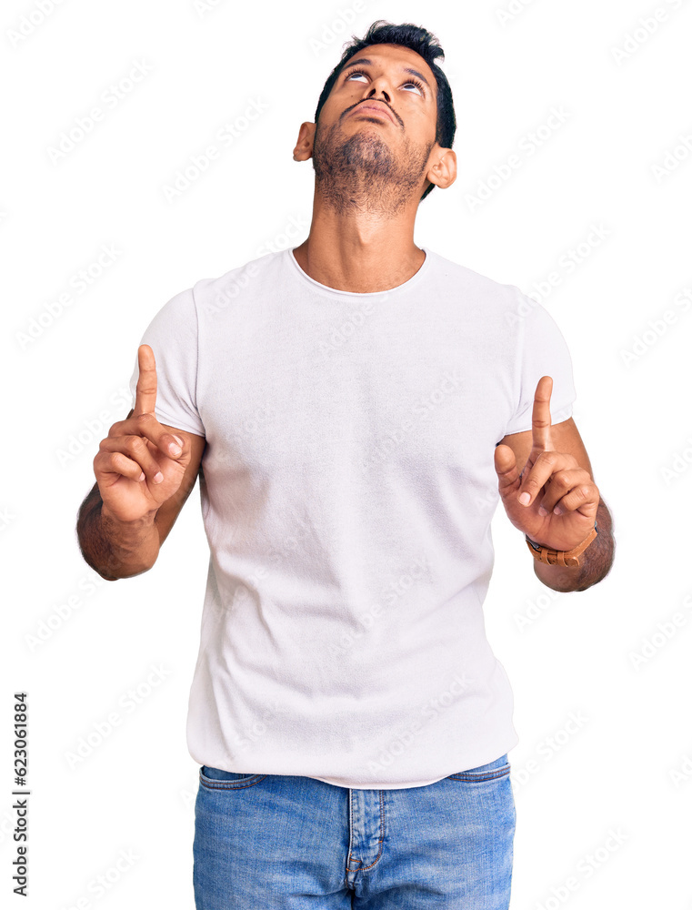 Fototapeta premium Young latin man wearing casual clothes pointing up looking sad and upset, indicating direction with fingers, unhappy and depressed.