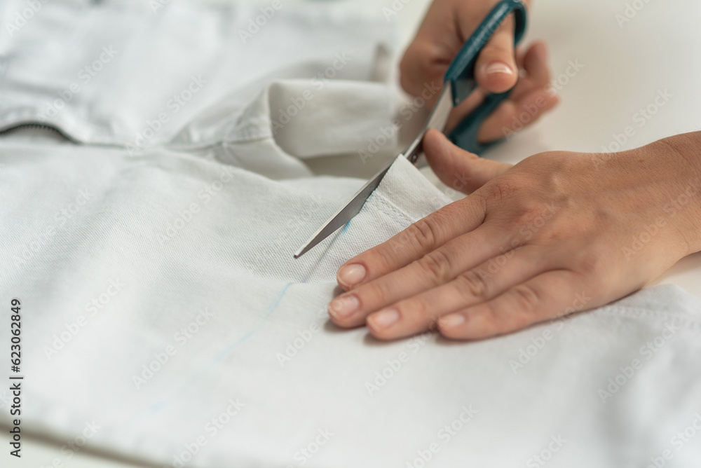 Shortening jeans. White jeans, Measuring tape, scissors on table. Jeans cutting. Shortening jeans. White jeans, Measuring tape, scissors on table. Jeans cutting.
