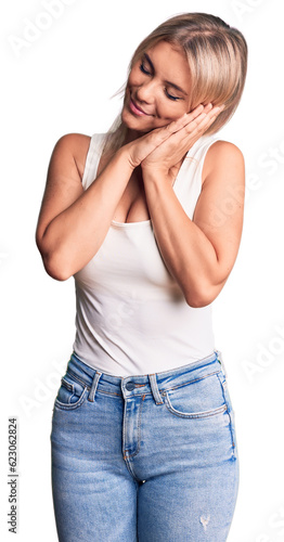 Young beautiful blonde woman wearing casual sleeveless t-shirt sleeping tired dreaming and posing with hands together while smiling with closed eyes.