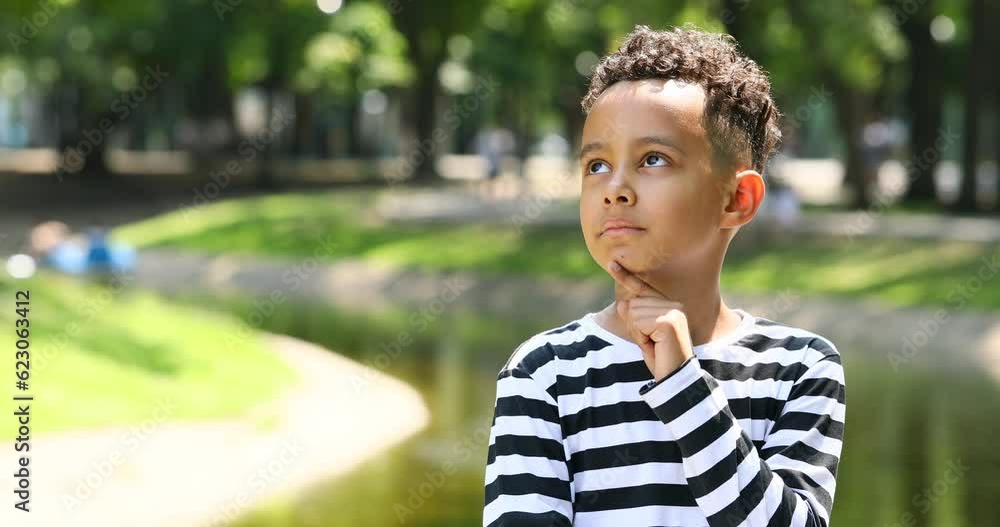 Cute pensive little boy in a striped t-shirt in a summer park Cute pensive little boy in a striped t-shirt in a summer park