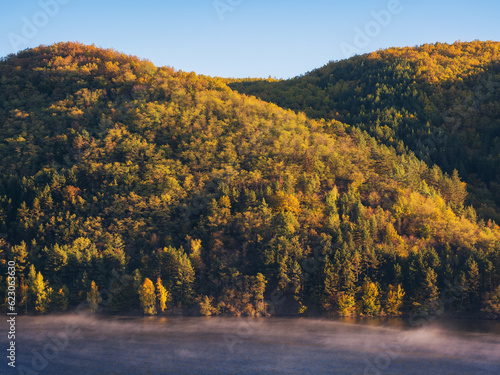 mountainous autumn landscape with lake. nature background with trees on the shore in fall colors. warm sunny weather