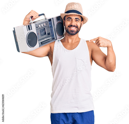 Young hispanic man holding boombox, listening to music pointing finger to one self smiling happy and proud