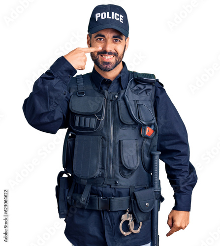 Young hispanic man wearing police uniform pointing with hand finger to face and nose, smiling cheerful. beauty concept