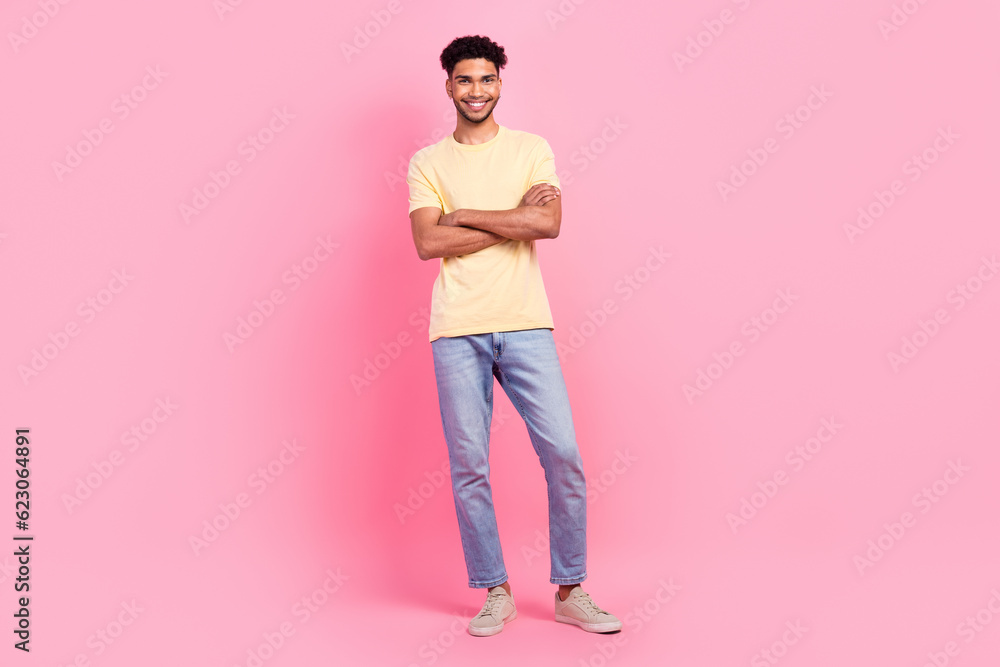 Full length photo of satisfied pleasant friendly guy wear yellow shirt standing holding arms crossed isolated on pink color background Full length photo of satisfied pleasant friendly guy wear yellow shirt standing holding arms crossed isolated on pink color background