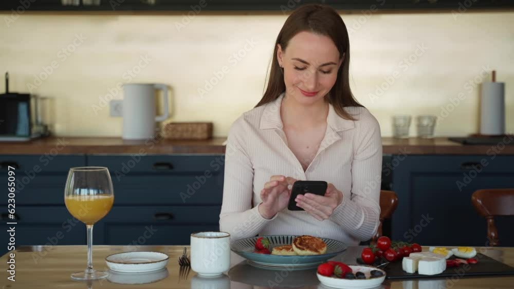 Happy woman uses a smartphone in the kitchen during a healthy breakfast in the morning, enjoys the weekend at home Happy woman uses a smartphone in the kitchen during a healthy breakfast in the morning, enjoys the weekend at home