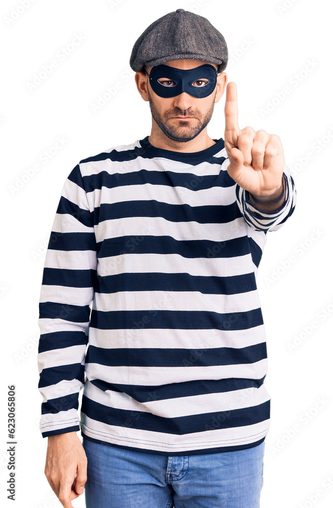 Young handsome man wearing burglar mask pointing with finger up and angry expression, showing no gesture Young handsome man wearing burglar mask pointing with finger up and angry expression, showing no gesture