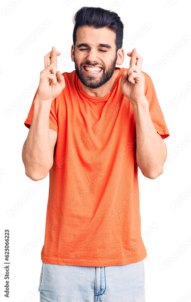 Young handsome man with beard wearing casual t-shirt gesturing finger crossed smiling with hope and eyes closed. luck and superstitious concept. Young handsome man with beard wearing casual t-shirt gesturing finger crossed smiling with hope and eyes closed. luck and superstitious concept.