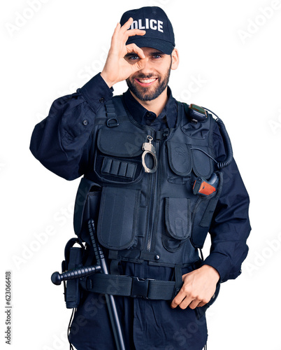 Young handsome man with beard wearing police uniform doing ok gesture with hand smiling, eye looking through fingers with happy face. © Krakenimages.com