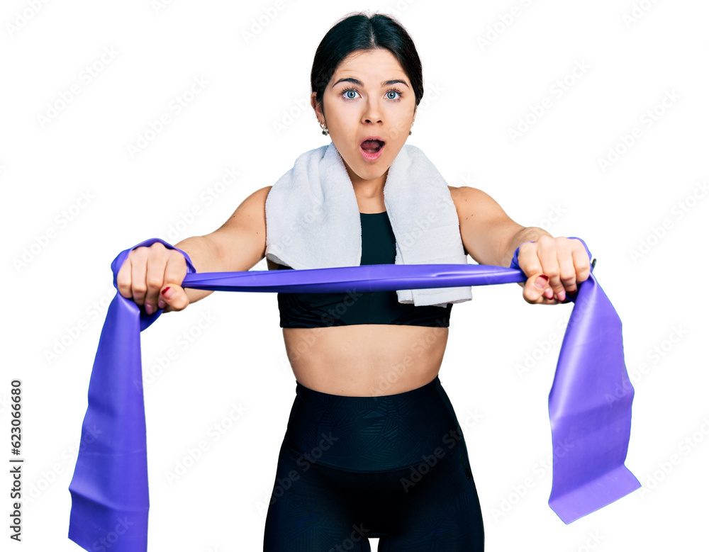 Young brunette woman with blue eyes training arm resistance with elastic arm bands afraid and shocked with surprise and amazed expression, fear and excited face. Young brunette woman with blue eyes training arm resistance with elastic arm bands afraid and shocked with surprise and amazed expression, fear and excited face.
