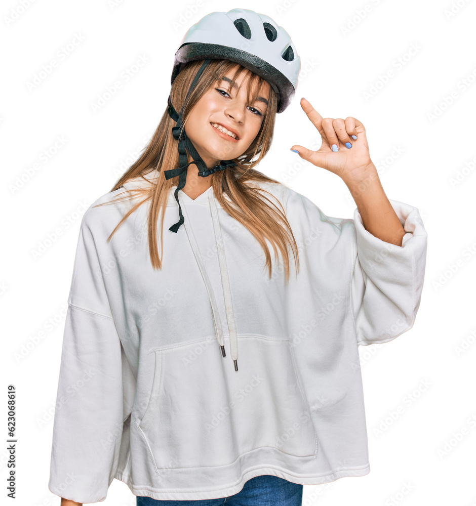 Teenager caucasian girl wearing bike helmet smiling and confident gesturing with hand doing small size sign with fingers looking and the camera. measure concept. Teenager caucasian girl wearing bike helmet smiling and confident gesturing with hand doing small size sign with fingers looking and the camera. measure concept.