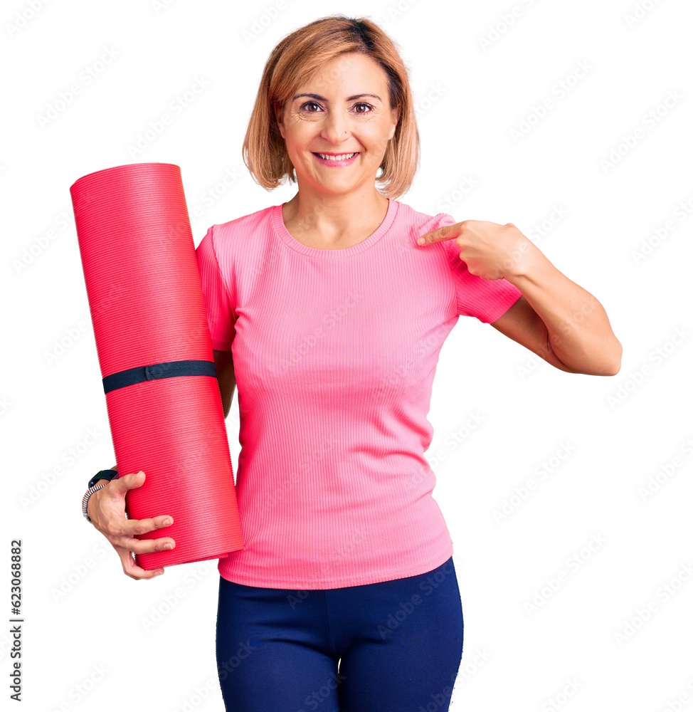 Young blonde woman holding yoga mat pointing finger to one self smiling happy and proud Young blonde woman holding yoga mat pointing finger to one self smiling happy and proud