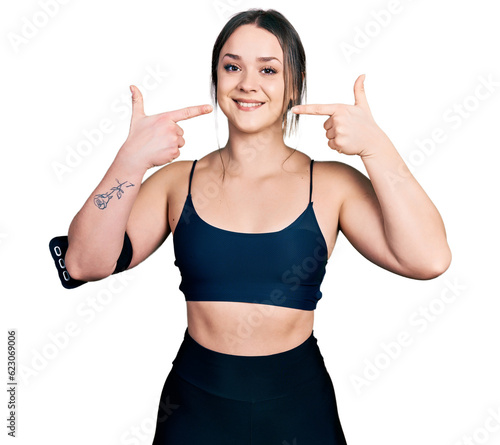 Young hispanic woman wearing sportswear smiling cheerful showing and pointing with fingers teeth and mouth. dental health concept.