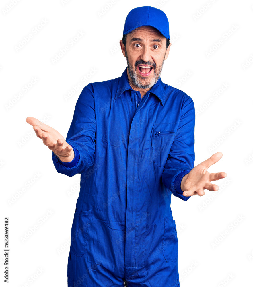 Middle age handsome man wearing mechanic uniform smiling cheerful with open arms as friendly welcome, positive and confident greetings Middle age handsome man wearing mechanic uniform smiling cheerful with open arms as friendly welcome, positive and confident greetings