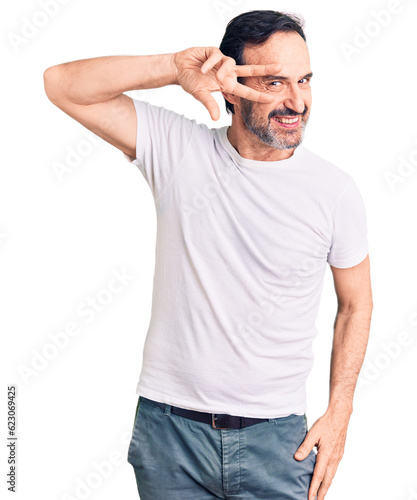 Middle age handsome man wearing casual t-shirt doing peace symbol with fingers over face  smiling cheerful showing victory