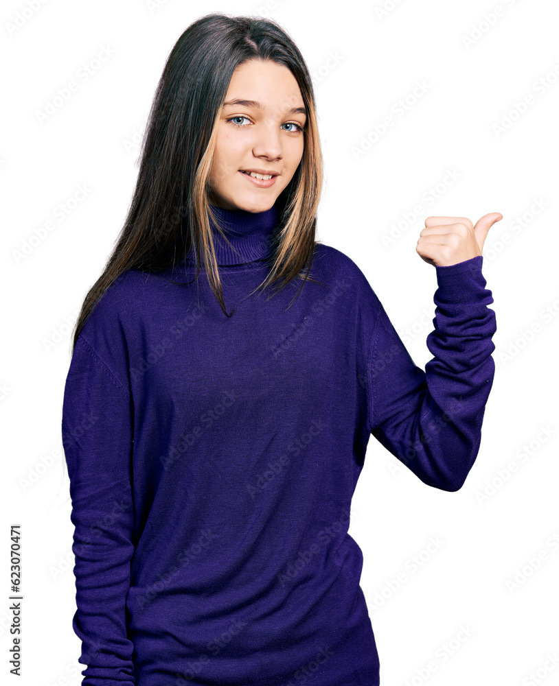 Young brunette girl with long hair wearing turtleneck sweater smiling with happy face looking and pointing to the side with thumb up. Young brunette girl with long hair wearing turtleneck sweater smiling with happy face looking and pointing to the side with thumb up.