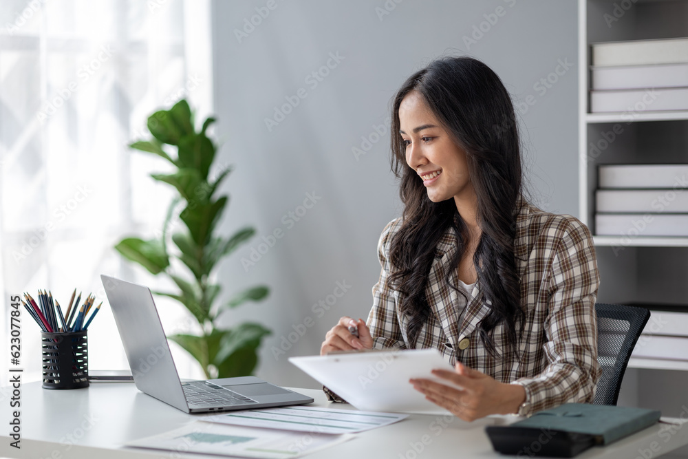 A beautiful Asian businesswoman sitting in her private office, she is checking company financial documents, she is a female executive of a startup company. Concept of financial management. A beautiful Asian businesswoman sitting in her private office, she is checking company financial documents, she is a female executive of a startup company. Concept of financial management.